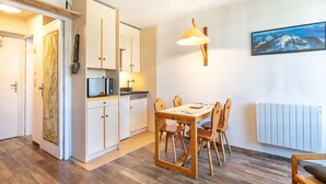 Una cocina compacta con armarios blancos, una mesa de comedor con sillas, una lámpara colgante y un cuadro en la pared.