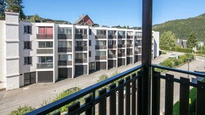 Un edificio moderno de varios pisos con balcones, un estacionamiento y vistas a un paisaje montañoso.