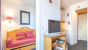 A small, cozy room with a wooden bed, a television on a wooden stand, and a white door. - Peaceful Alpine Escape, Risoul (Risoul)