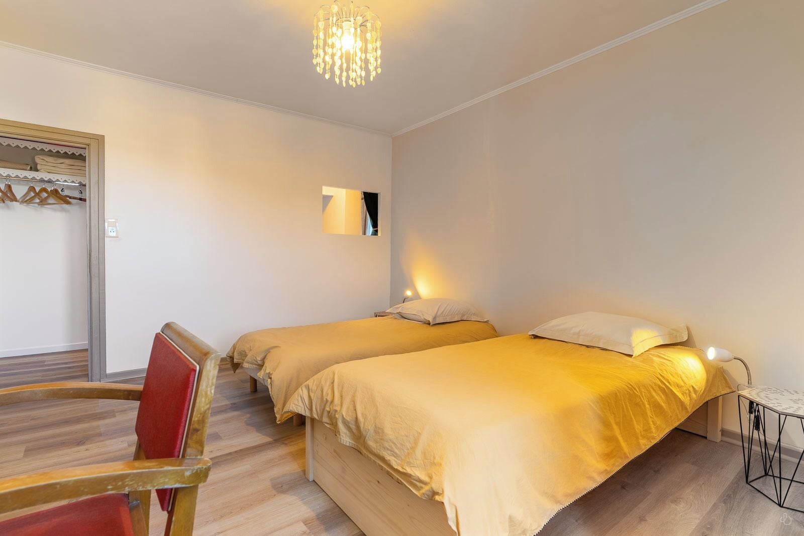 A room with two beds, a chair, a table, and a chandelier.