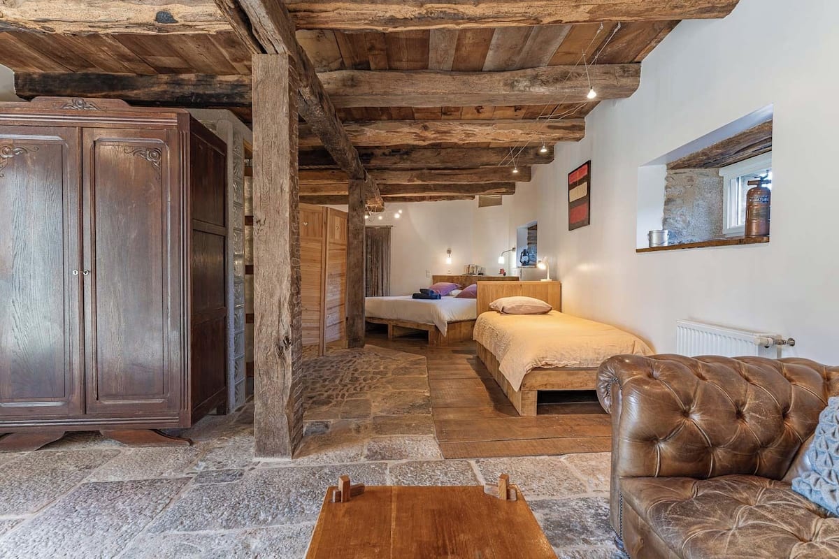 Une pièce rustique avec un plafond en bois, une grande armoire, un lit avec une tête de lit, un canapé en cuir et un sol en pierre.