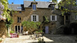 A stone building with a courtyard, featuring a small tree, outdoor seating, and a staircase leading to an upper level. - Le Clos du Barry (Laissac-Severac-l'Eglise)