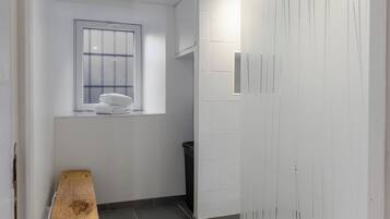 Um corredor com um banco de madeira, uma janela, uma lixeira e um guarda-roupa branco.