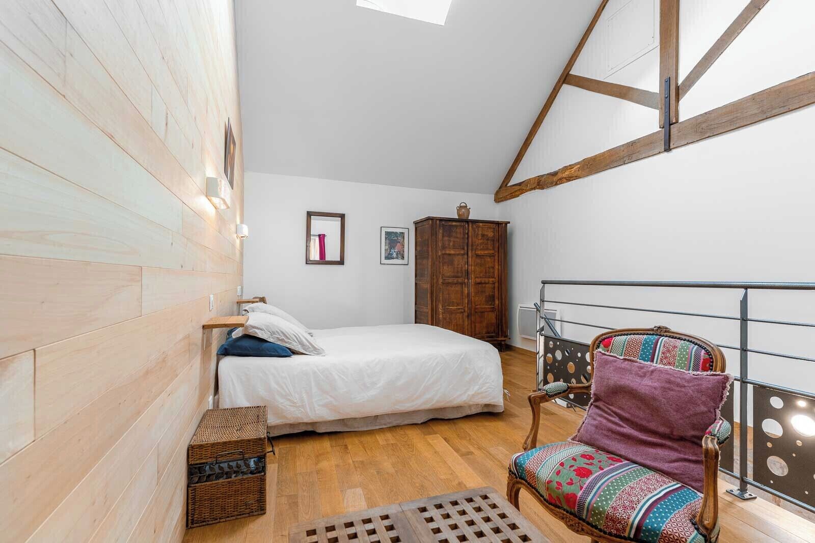 Quarto com cama, guarda-roupa de madeira, cesta de vime, cadeira com almofada estampada e corrimão de metal.