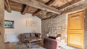 A rustic room with exposed wooden beams, a stone wall, a leather sofa, a wooden coffee table, and a wooden door. - Le Clos du Barry (Laissac-Severac-l'Eglise)