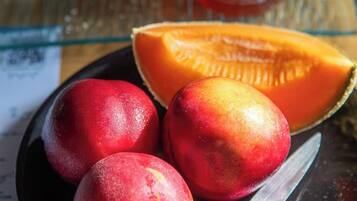 A plate with three peaches and a half-cut cantaloupe, a knife, and a jar of honey on a table.