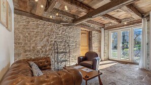 A rustic room with exposed stone walls, a leather sofa, a wooden coffee table, and a large window with a view of the outdoors. - Le Clos du Barry (Laissac-Severac-l'Eglise)