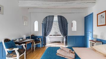 A room with a bathtub, a chair, a table, and a bed.