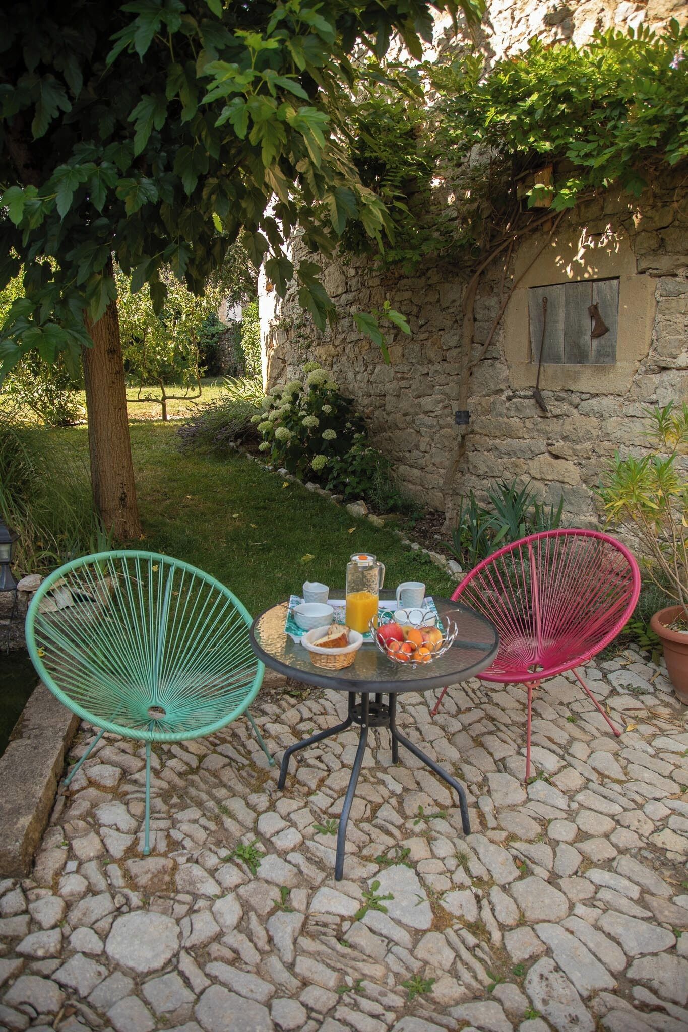 A patio with two chairs, a table, and a stone wall in the background.