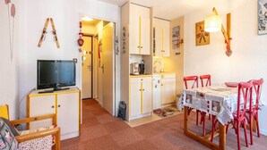 Ett kompakt bostadsutrymme med tv, pentry, matplats och en hall som leder till ett annat rum.
