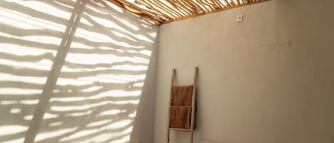 A room with a bamboo ceiling, a towel hanging on a rack, and a stone bench.