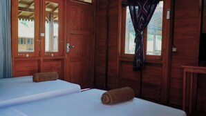 A wooden room with two beds, a window with curtains, and a view of a building outside.