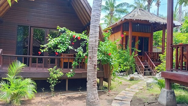 A wooden house with a balcony, a thatched-roof structure, and a stone pathway.