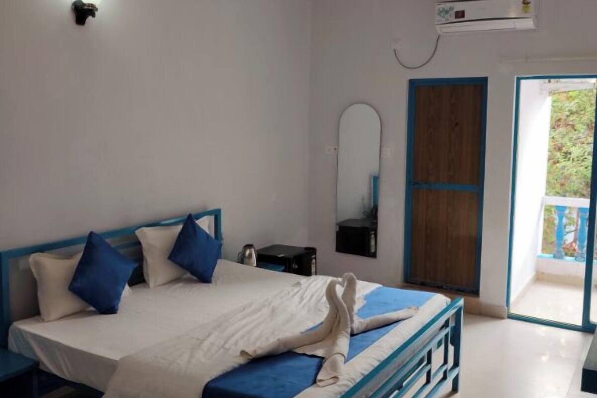 Una camera da letto con un letto, una ventola a soffitto, un condizionatore d'aria, uno specchio e una porta che dà su un balcone esterno.