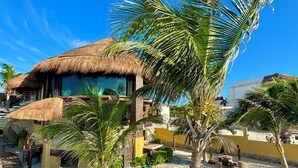 Une propriété située en bord de mer, avec un bâtiment à toit de chaume, des palmiers et un sentier sablonneux.