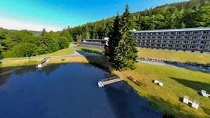 Un grand bâtiment à étages, un plan d’eau devant et une colline boisée en arrière-plan.