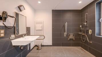 A modern bathroom with a white sink, a hairdryer, a towel rack, and a shower with a handheld showerhead.