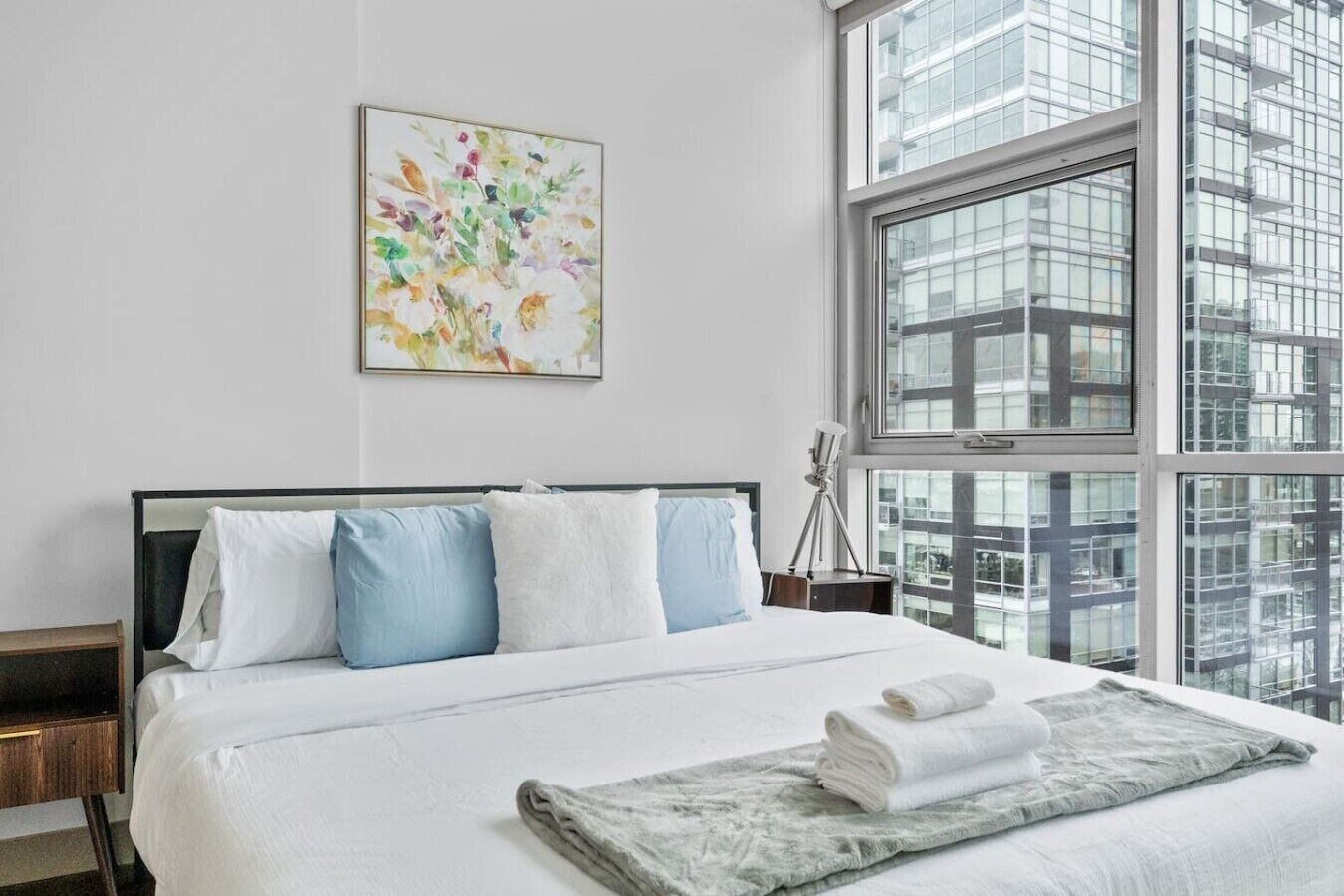 A hotel room with a large bed, a telescope, and a city view through the window.