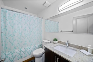 Un baño con cortina de ducha, inodoro, lavamanos, espejo y una pequeña planta en maceta.