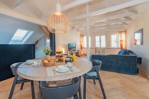 A dining area with a round table set for four, a hanging light fixture, and a view of the living room in the background. - Baltic House 05 - Exclusive loft ambience in Heringsdorf (Heringsdorf (Seebad))