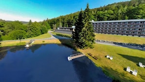 A large building with multiple floors, a body of water in front, and a forested hill in the background.