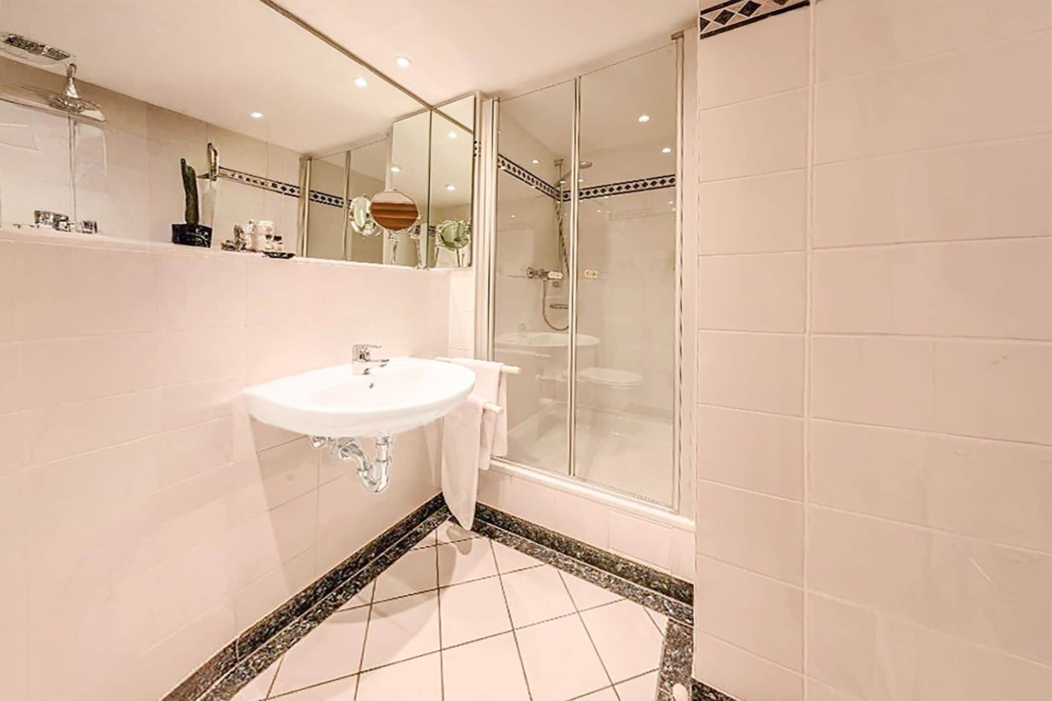 Ein modernes Badezimmer mit einem weißen Waschbecken, einem großen Spiegel und einer Duschkabine.