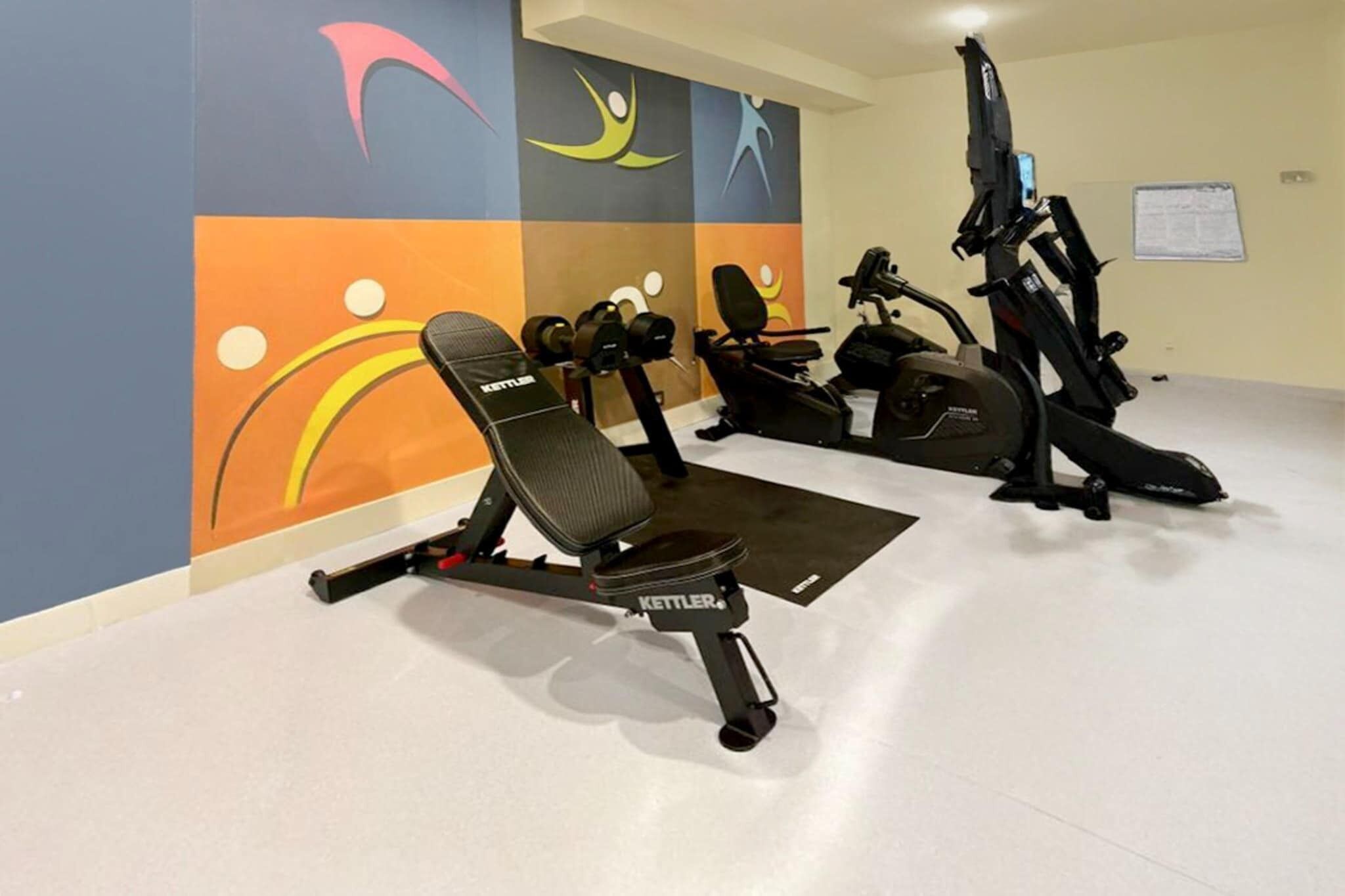 Ein Fitnessraum mit einer Kettler-Bank, einem Rudergerät und einem Crosstrainer.
