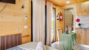 A wooden cabin room with a bed, a small table with glasses and a menu, a chair, and a door leading to a balcony. - Minicasa La Barca (Ascea)