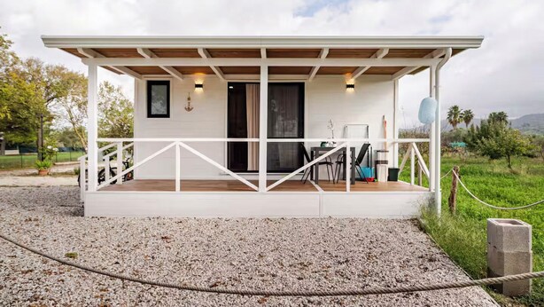 A white building with a wooden deck, a table with chairs, and a door. - Minicasa La Barca (Ascea)