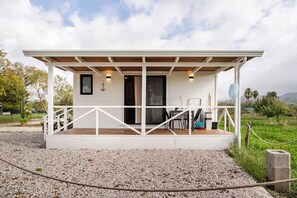 A white building with a wooden deck, a table with chairs, and a door. - Minicasa La Barca (Ascea)