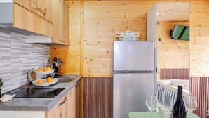 A compact kitchen with wooden cabinets, a stainless steel refrigerator, and a small dining area with a table and chairs. - Minicasa La Barca (Ascea)