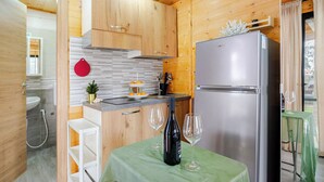 A compact kitchen with wooden cabinets, a stainless steel refrigerator, and a small dining area with a table set for two. - Minicasa La Barca (Ascea)