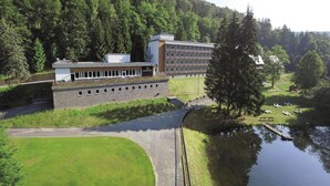 A modern building with a flat roof, a stone wall, and a grassy area with a pond.