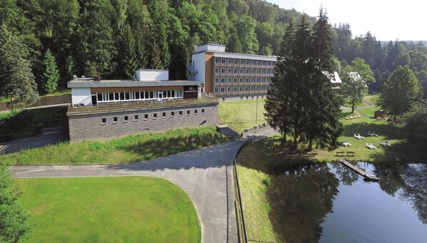 A modern building with a flat roof, a stone wall, and a grassy area with a pond.