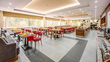 A spacious restaurant with multiple dining tables and red chairs, large windows, and a modern interior design.