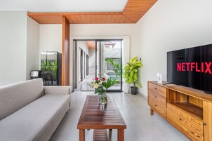 Una sala de estar moderna con un sofá, una mesa de centro de madera, un televisor y un ventanal corredizo que da a un balcón.