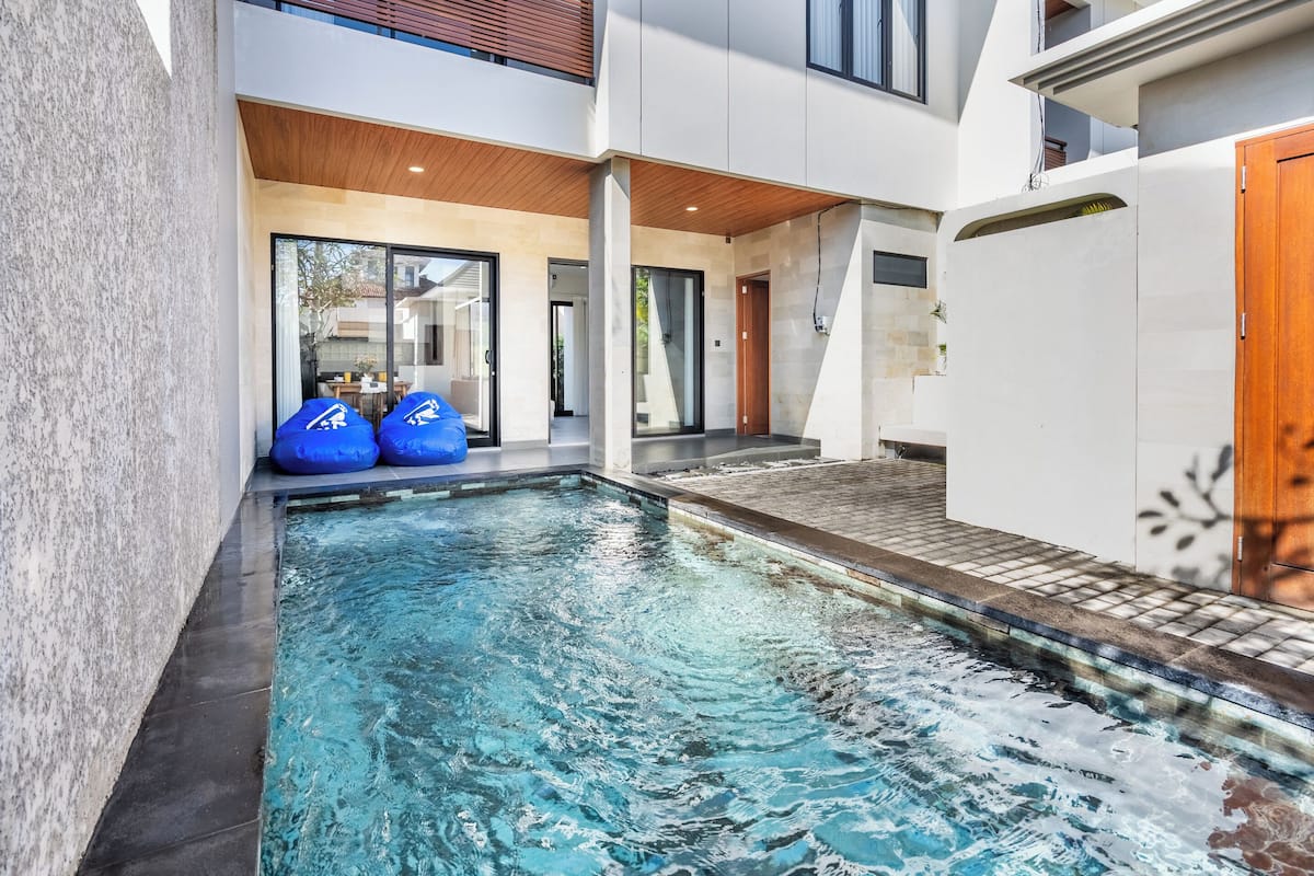 Un espace piscine moderne avec une eau cristalline, un plafond en bois et un mur extérieur blanc.