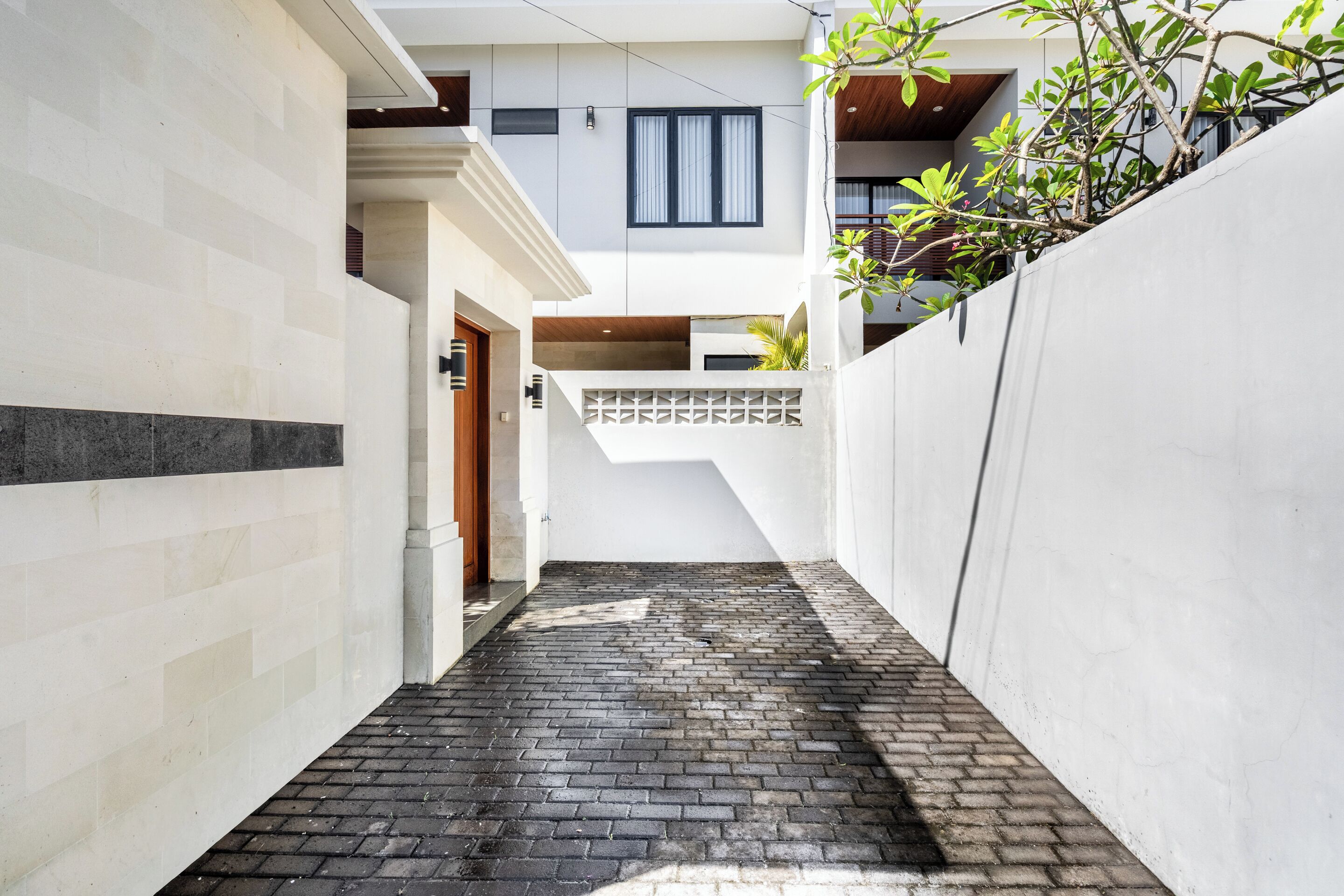 A narrow brick pathway leading to a building with a white facade and a small window.