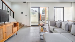 A modern living room with a sofa, TV, wooden cabinet, and a table with a vase of flowers. - Cendana Villa Sanur (Denpasar)