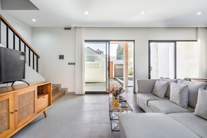 Una sala de estar moderna con un sofá, televisor, mueble de madera y una mesa con un jarrón de flores.