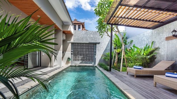 A swimming pool with a wooden deck, lounge chairs, and tropical plants. - Cendana Villa Sanur (Denpasar)