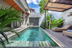 Una piscina con muelle de madera, sillas de descanso y plantas tropicales.