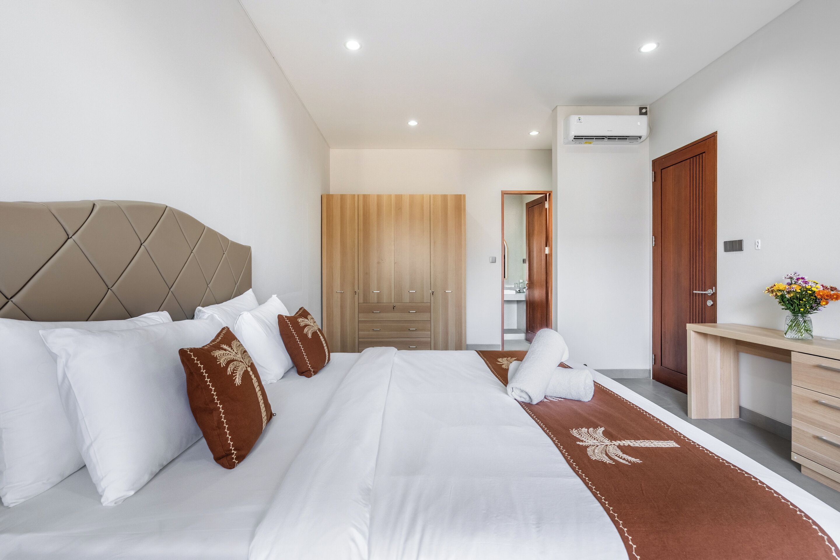 A modern hotel room with a large bed, a wooden wardrobe, a desk, and an air conditioning unit.