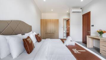 A modern hotel room with a large bed, a wooden wardrobe, a desk, and an air conditioning unit.