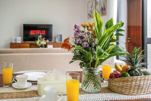 Un comedor con una mesa dispuesta para el desayuno, que incluye platos, tazas y un jarrón con flores.