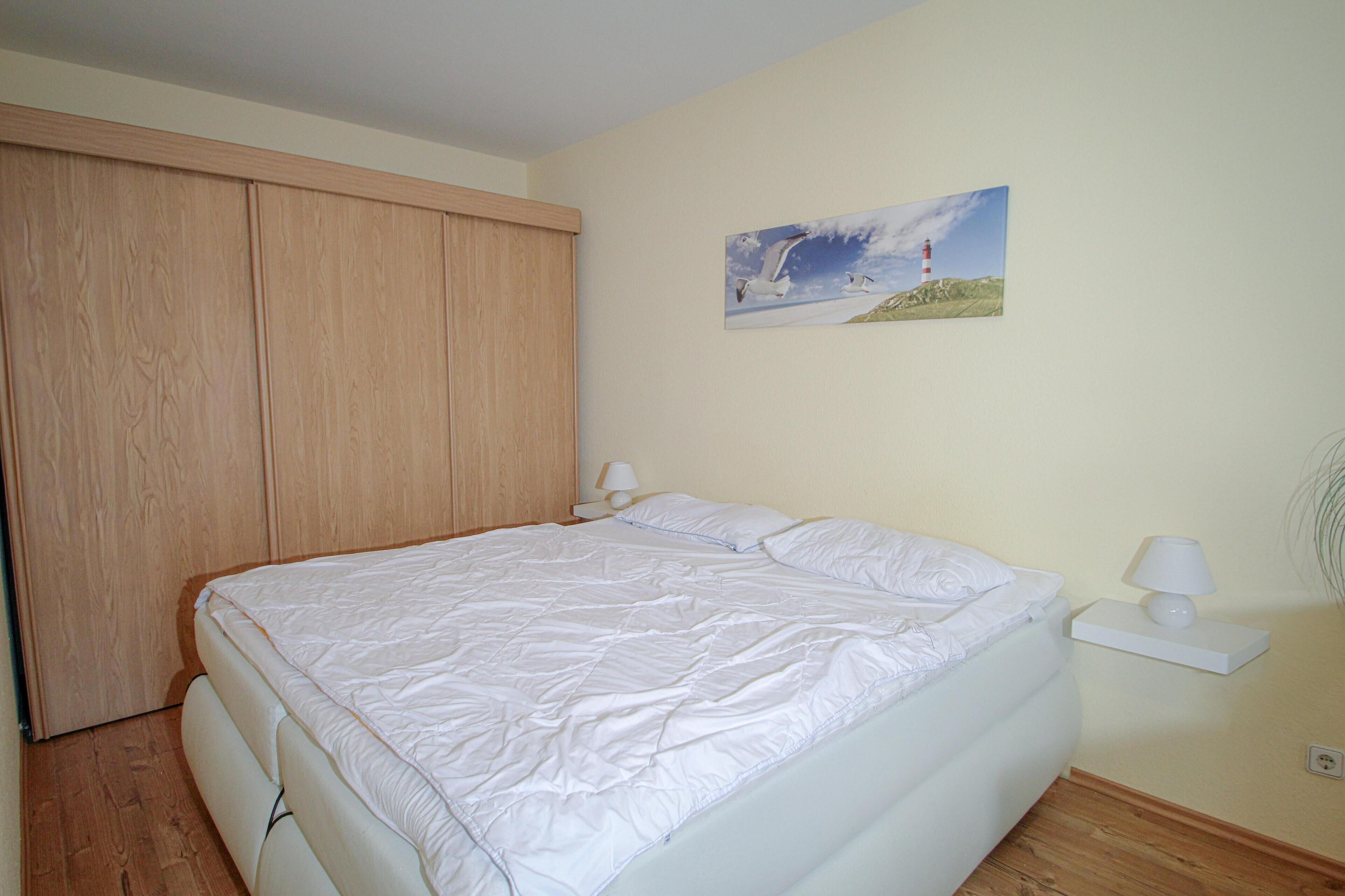 A bedroom with a large bed, wooden wardrobe, and a painting of a lighthouse on the wall.