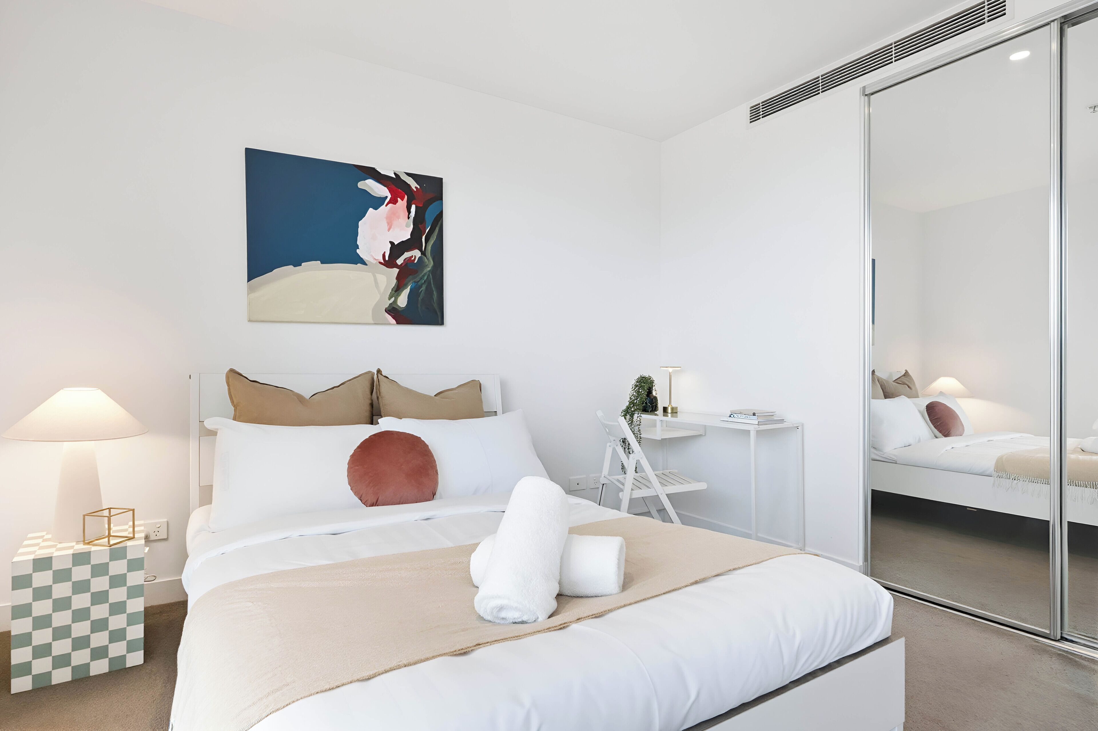 Een moderne hotelkamer met een bed, nachtkastje, lamp, klein bijzettafeltje en een grote spiegel.