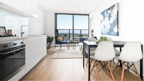 Eine moderne Küche mit weißen Schränken, einem großen Fenster und einem Essbereich mit weißen Stühlen und einem Tisch.