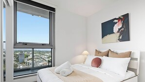 Ein modernes Hotelzimmer mit großem Fenster, einem Bett mit weißer Bettwäsche und Blick auf die Stadt.