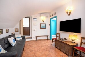 A living room with a black leather sofa, a wooden bench, a TV mounted on the wall, and a lamp on a wooden table. - Gaiano APT (Sorrento)